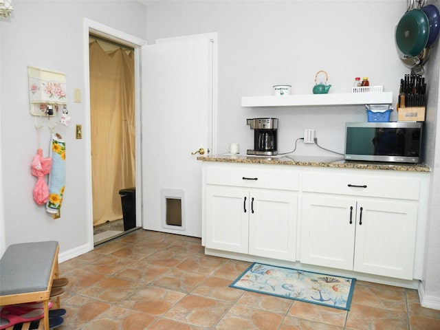 kitchen with open shelves, light stone counters, stainless steel microwave, and white cabinetry