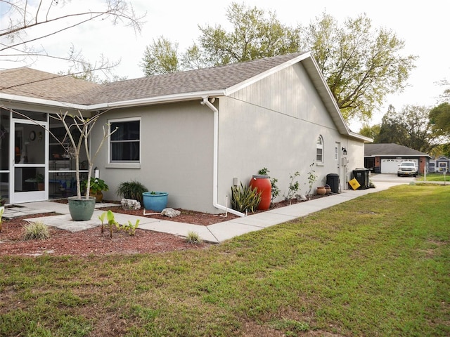 view of home's exterior featuring stucco siding, a shingled roof, a lawn, a sunroom, and a garage