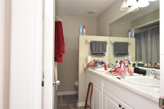 bathroom with double vanity, visible vents, toilet, a sink, and baseboards