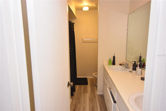 full bath featuring double vanity, baseboards, toilet, wood finished floors, and a sink