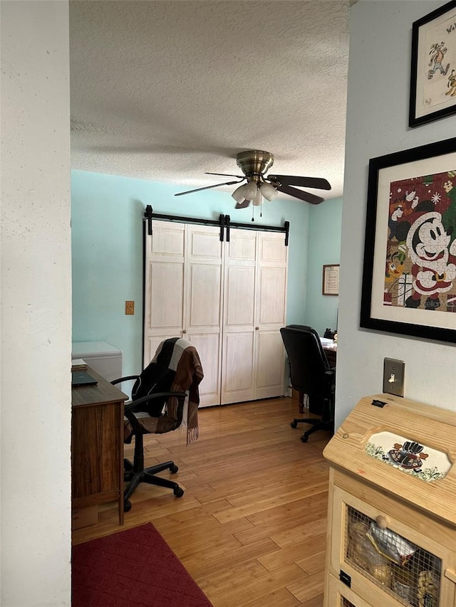 office featuring ceiling fan, a barn door, a textured ceiling, and light wood-type flooring