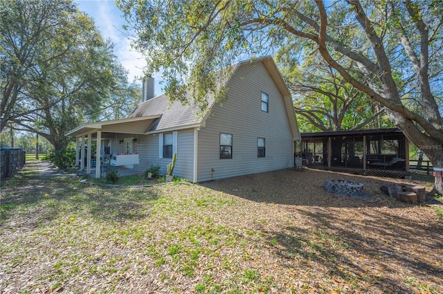 back of house featuring covered porch, roof with shingles, a lawn, and a chimney