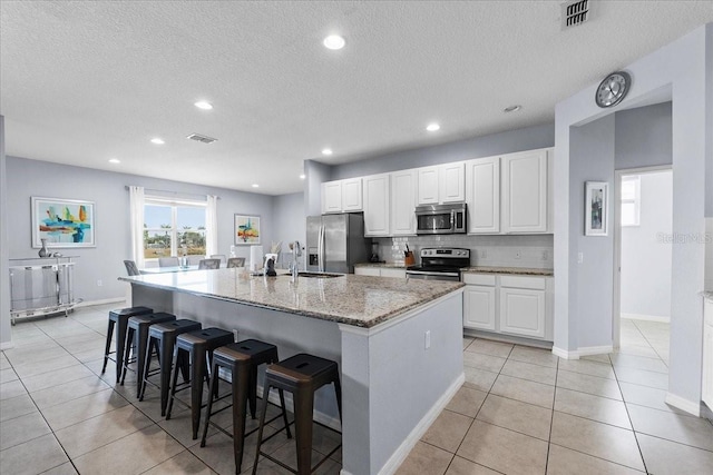 kitchen featuring a breakfast bar area, stainless steel appliances, visible vents, white cabinets, and an island with sink