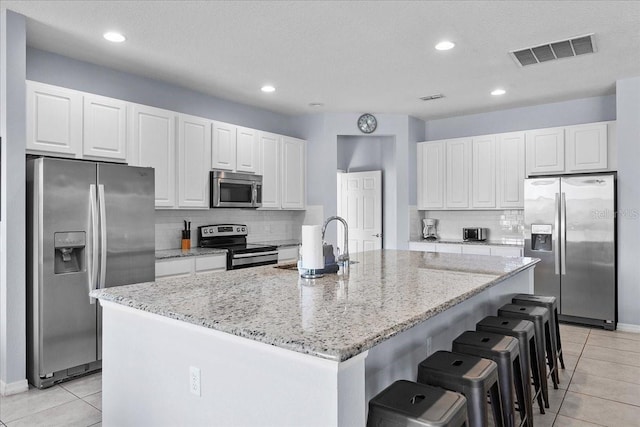 kitchen with an island with sink, white cabinetry, visible vents, and appliances with stainless steel finishes