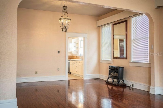 spare room with an inviting chandelier, dark hardwood / wood-style flooring, sink, and a wood stove