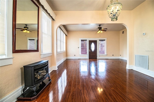 foyer with dark hardwood / wood-style flooring, ceiling fan with notable chandelier, and a wood stove