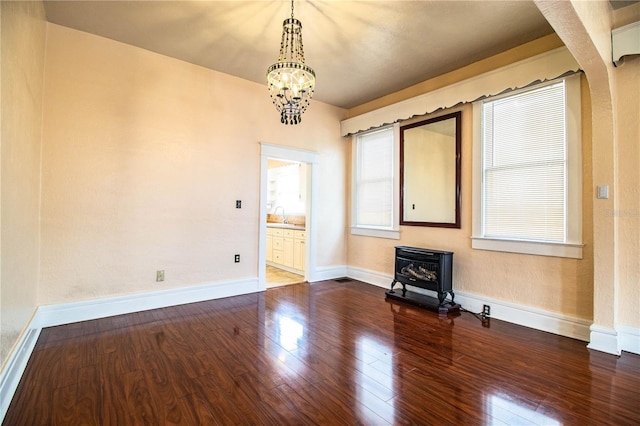 unfurnished living room with sink, wood-type flooring, a chandelier, and a wood stove