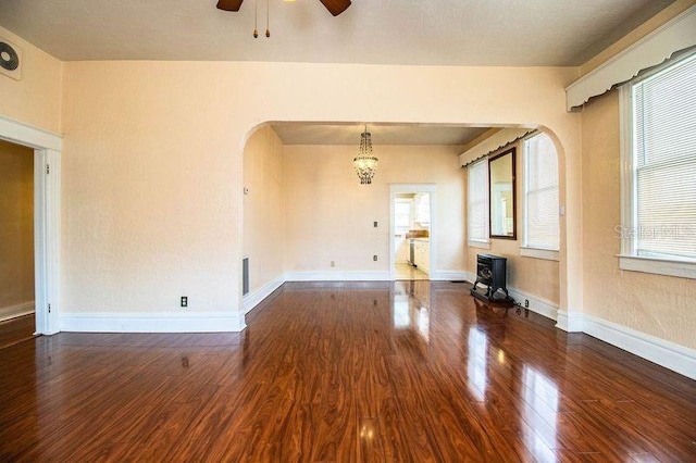 unfurnished room featuring dark wood-type flooring, ceiling fan, and a wood stove