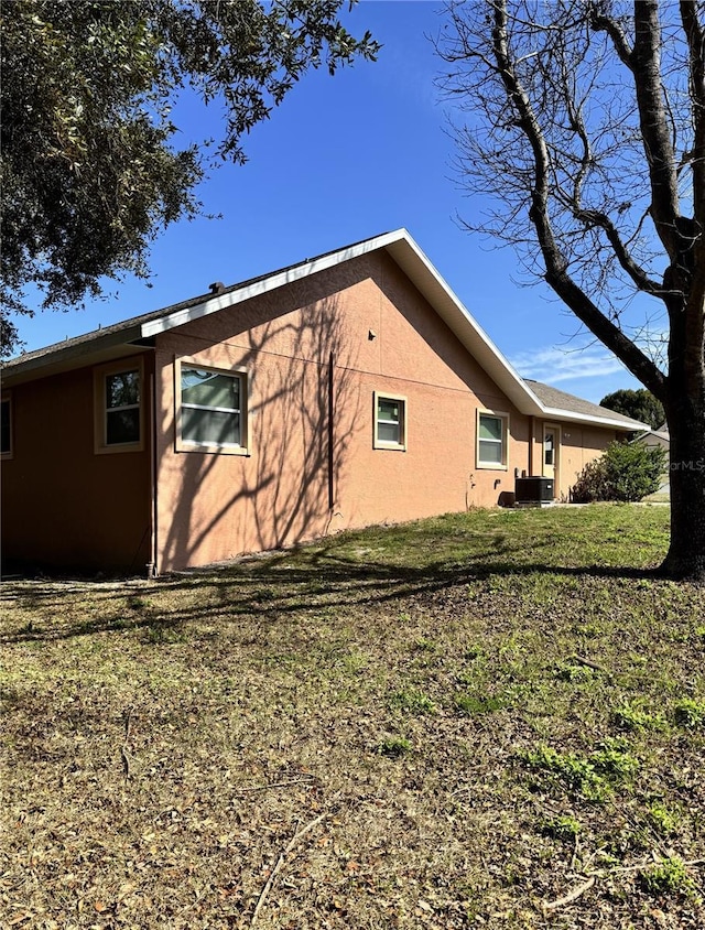 view of side of home with cooling unit, a yard, and stucco siding