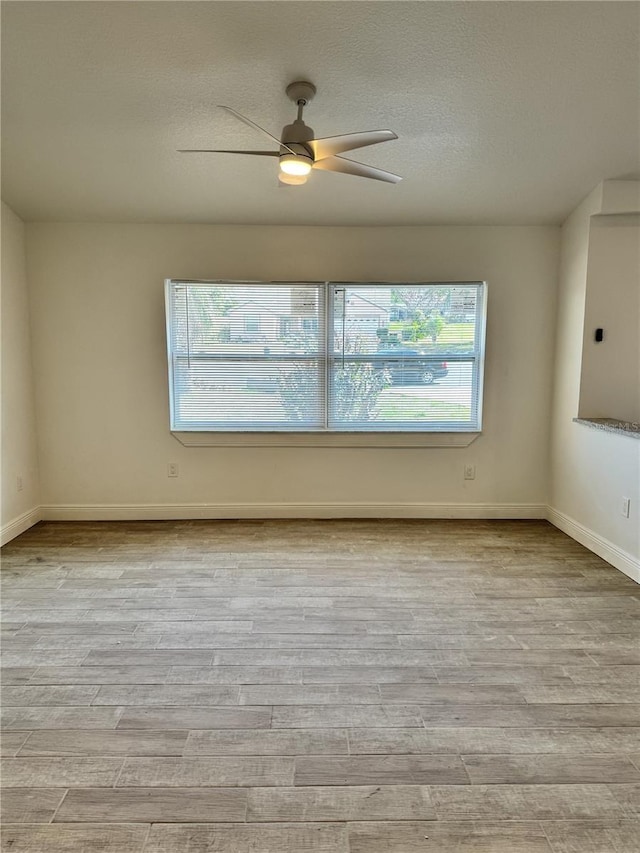 unfurnished room with a textured ceiling, ceiling fan, light wood-type flooring, and baseboards