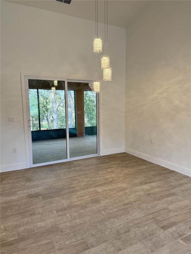 unfurnished room featuring light wood-style floors, baseboards, visible vents, and a high ceiling