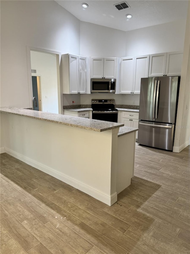 kitchen featuring visible vents, appliances with stainless steel finishes, white cabinetry, light stone countertops, and a peninsula