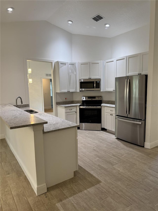 kitchen with stone countertops, a peninsula, visible vents, white cabinets, and appliances with stainless steel finishes