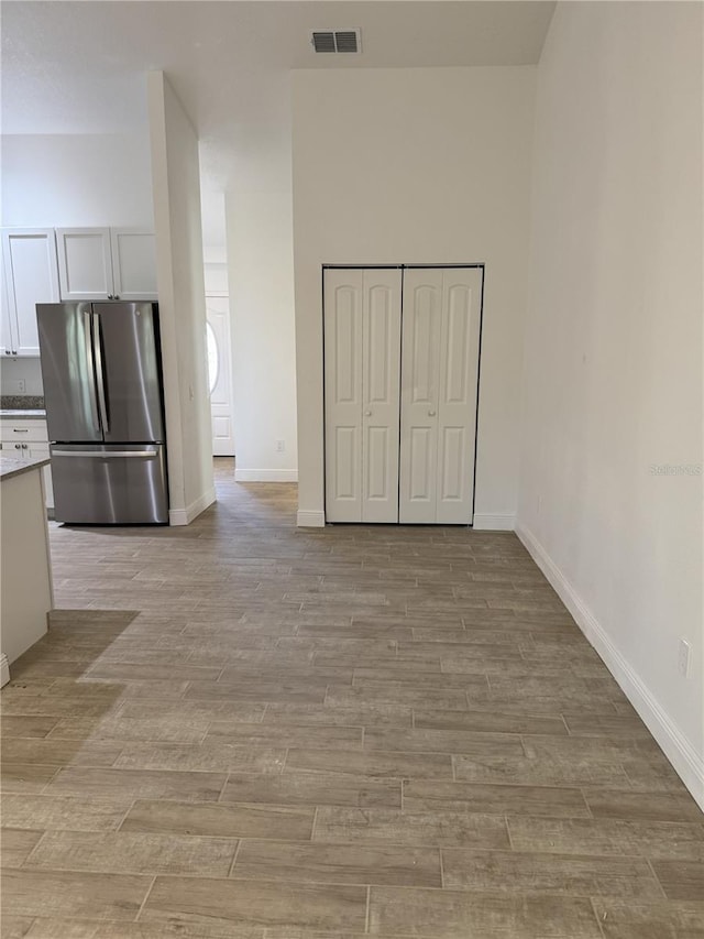 interior space with light wood-type flooring, baseboards, visible vents, and a high ceiling