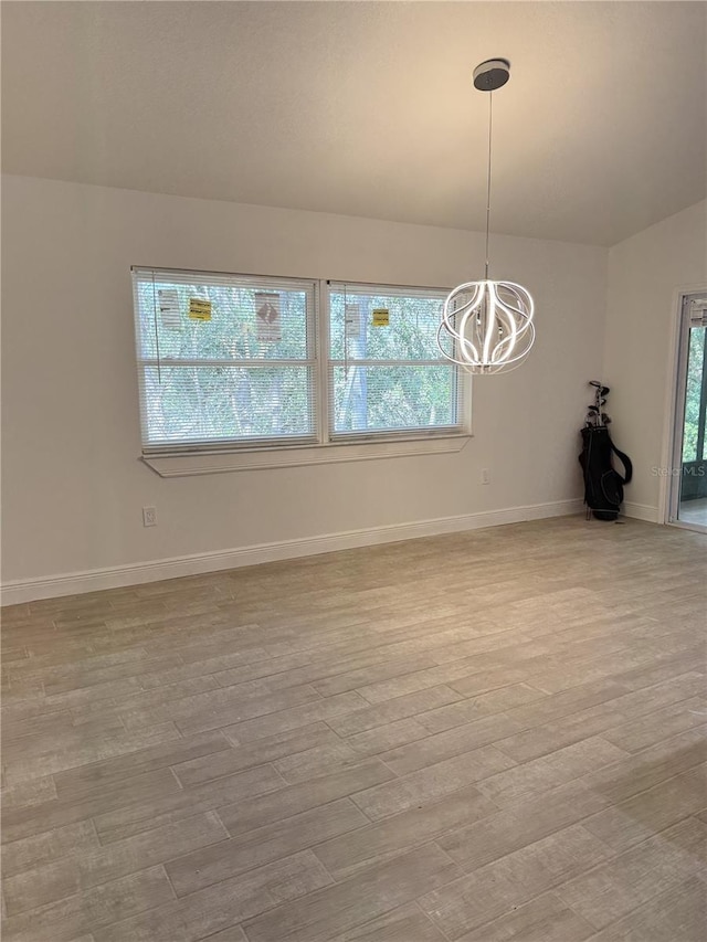 empty room featuring a healthy amount of sunlight, a notable chandelier, and light wood-style flooring