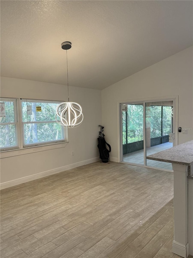 unfurnished dining area with a chandelier, lofted ceiling, a healthy amount of sunlight, and light wood finished floors