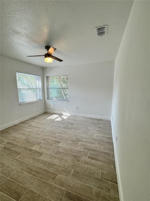 empty room featuring baseboards, wood tiled floor, visible vents, and a ceiling fan