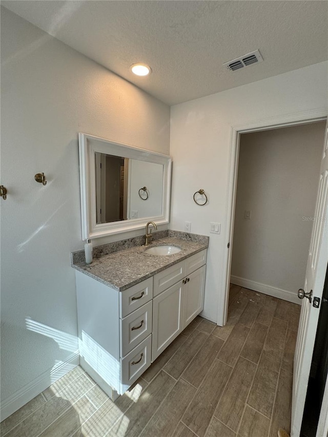 bathroom with a textured ceiling, wood finish floors, vanity, visible vents, and baseboards