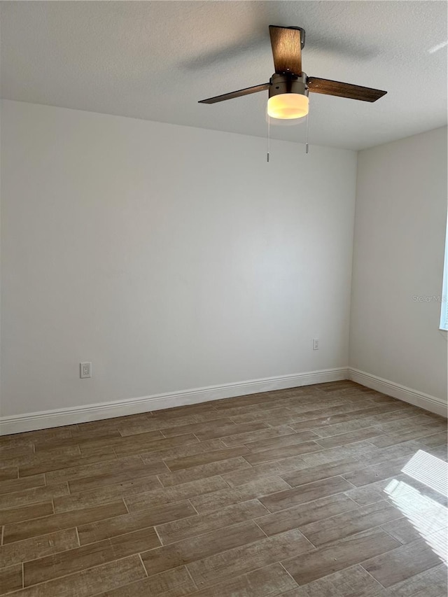 spare room with ceiling fan, a textured ceiling, baseboards, and wood finished floors