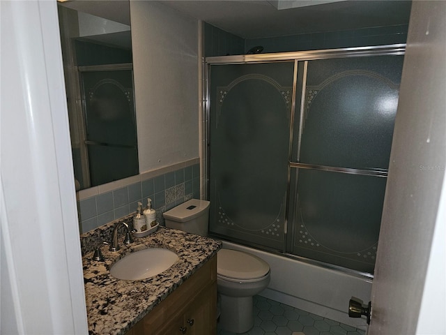 full bathroom with shower / bath combination with glass door, tile walls, tile patterned flooring, vanity, and toilet