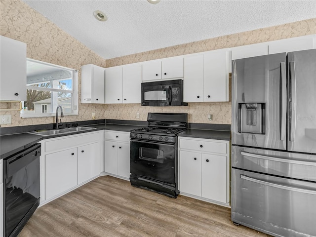 kitchen with dark countertops, white cabinetry, a sink, and black appliances