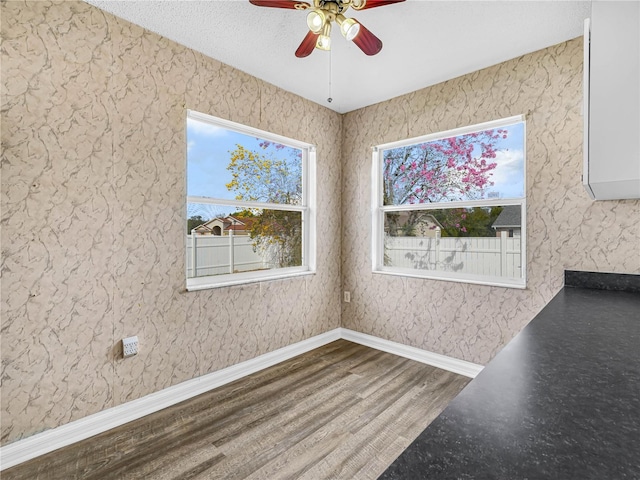 unfurnished dining area with a ceiling fan, baseboards, and wood finished floors