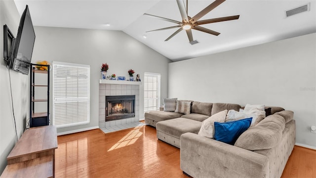 living room with a tiled fireplace, plenty of natural light, ceiling fan, and light wood-type flooring