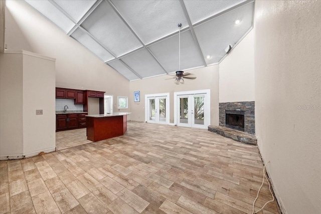 unfurnished living room featuring light hardwood / wood-style flooring, ceiling fan, plenty of natural light, a stone fireplace, and french doors