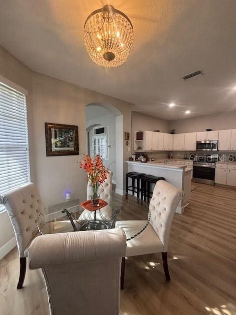 8623 Snowy Owl Way, Tampa, FL 33647 - dining area featuring visible vents, baseboards, arched walkways, a notable chandelier, and light wood-style flooring