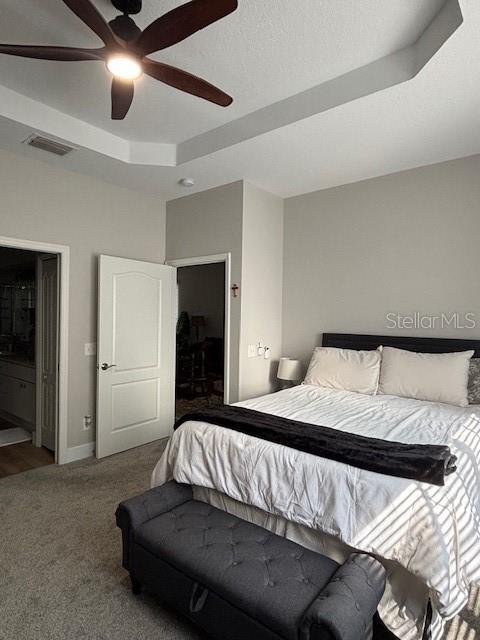 8623 Snowy Owl Way, Tampa, FL 33647 - carpeted bedroom with visible vents, baseboards, ceiling fan, a tray ceiling, and ensuite bath