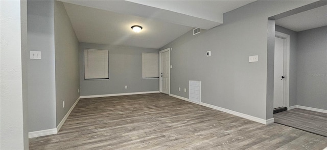 empty room with lofted ceiling, light wood finished floors, visible vents, and baseboards