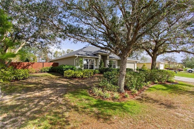 view of front facade featuring a garage, stucco siding, a front yard, and fence