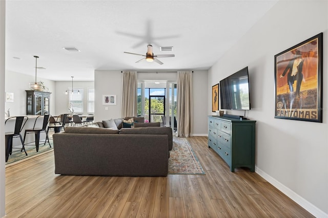 living area featuring visible vents, baseboards, light wood-style floors, and a ceiling fan