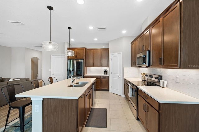 kitchen featuring a kitchen bar, visible vents, a sink, arched walkways, and appliances with stainless steel finishes