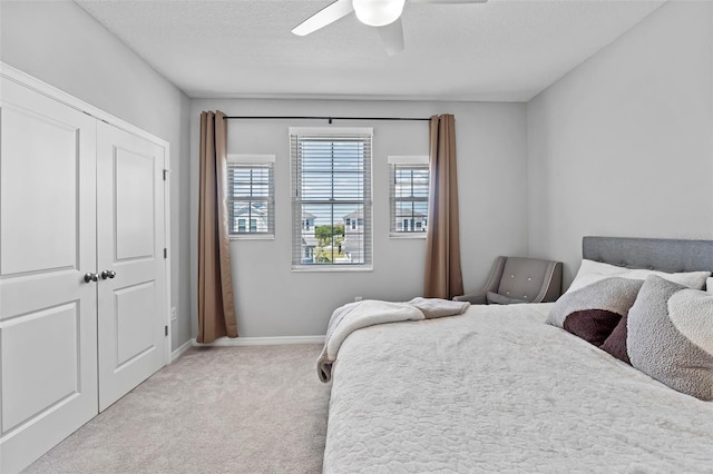 bedroom featuring baseboards, light carpet, a closet, a textured ceiling, and a ceiling fan