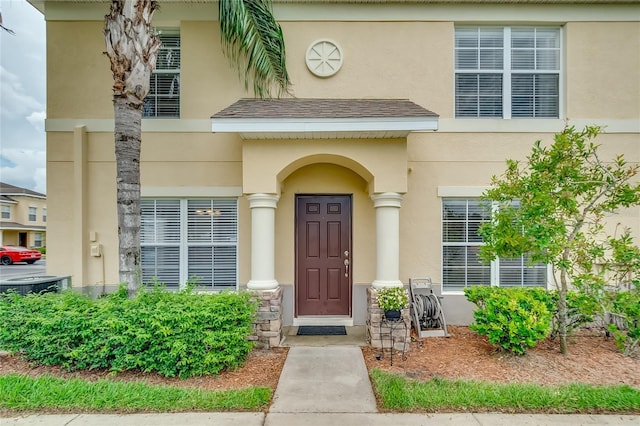 property entrance featuring central AC, a shingled roof, and stucco siding