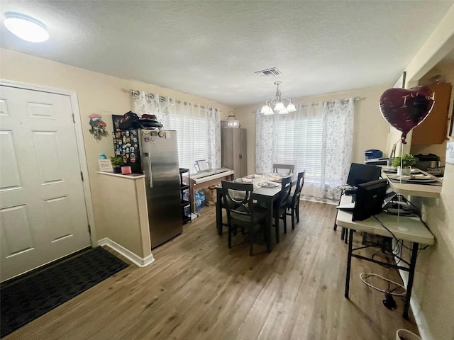 dining space featuring visible vents, an inviting chandelier, a textured ceiling, wood finished floors, and baseboards