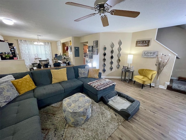 living room with a textured ceiling, ceiling fan with notable chandelier, wood finished floors, and baseboards