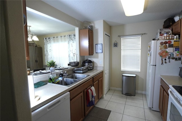 kitchen featuring light countertops, white appliances, brown cabinetry, and a sink