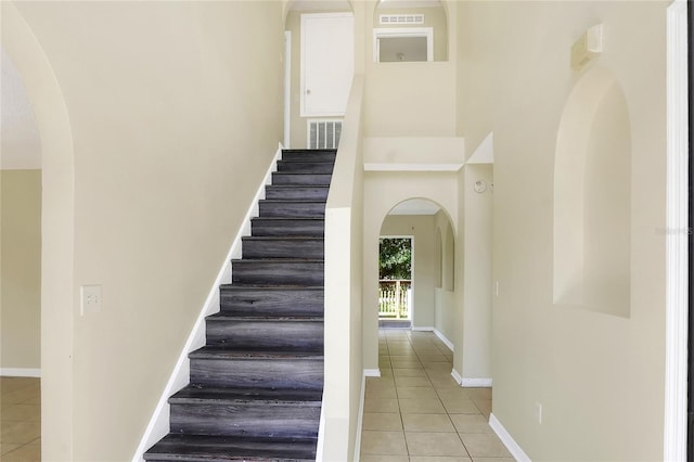 stairs with arched walkways, a towering ceiling, baseboards, tile patterned flooring, and visible vents