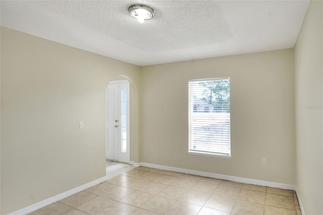 empty room with arched walkways, a textured ceiling, baseboards, and light tile patterned floors