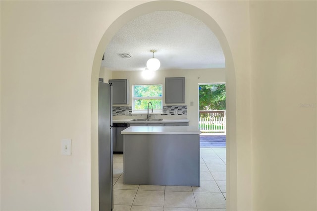 kitchen featuring stainless steel dishwasher, arched walkways, a sink, gray cabinetry, and light countertops
