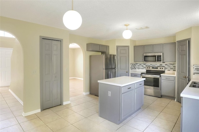 kitchen featuring a center island, decorative backsplash, arched walkways, stainless steel appliances, and gray cabinetry