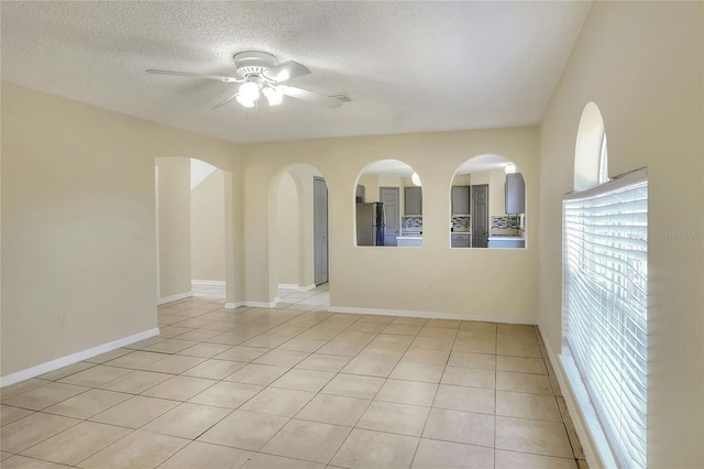 spare room with light tile patterned flooring, arched walkways, baseboards, a textured ceiling, and ceiling fan