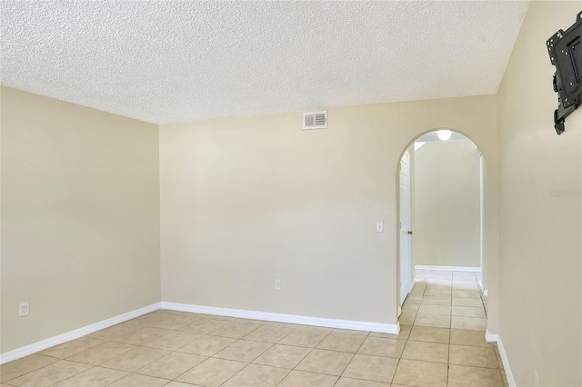 unfurnished room featuring arched walkways, a textured ceiling, visible vents, and light tile patterned floors