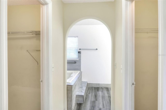 full bath with a spacious closet, a garden tub, and wood finished floors