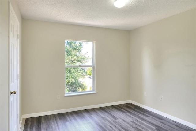 empty room with dark wood-type flooring, a textured ceiling, a wealth of natural light, and baseboards