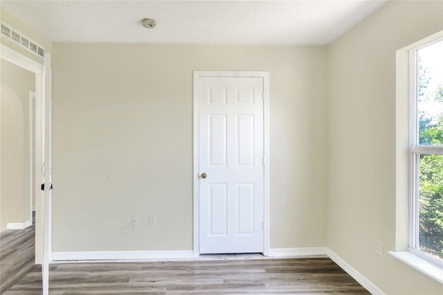 unfurnished bedroom with baseboards, wood finished floors, visible vents, and arched walkways