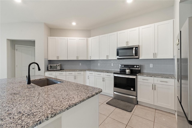 kitchen featuring white cabinets, decorative backsplash, light stone counters, stainless steel appliances, and a sink