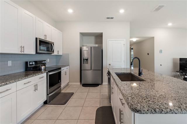 kitchen with a center island with sink, stainless steel appliances, visible vents, white cabinets, and a sink